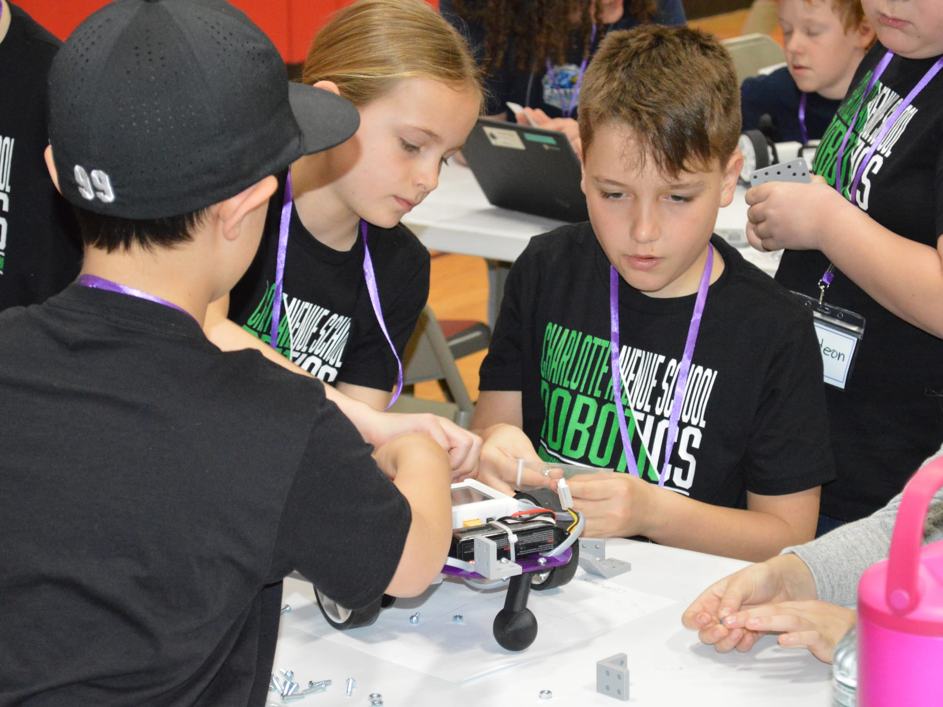 Three teammates in matching robotics shirts build a Pilot robot together at a competition table