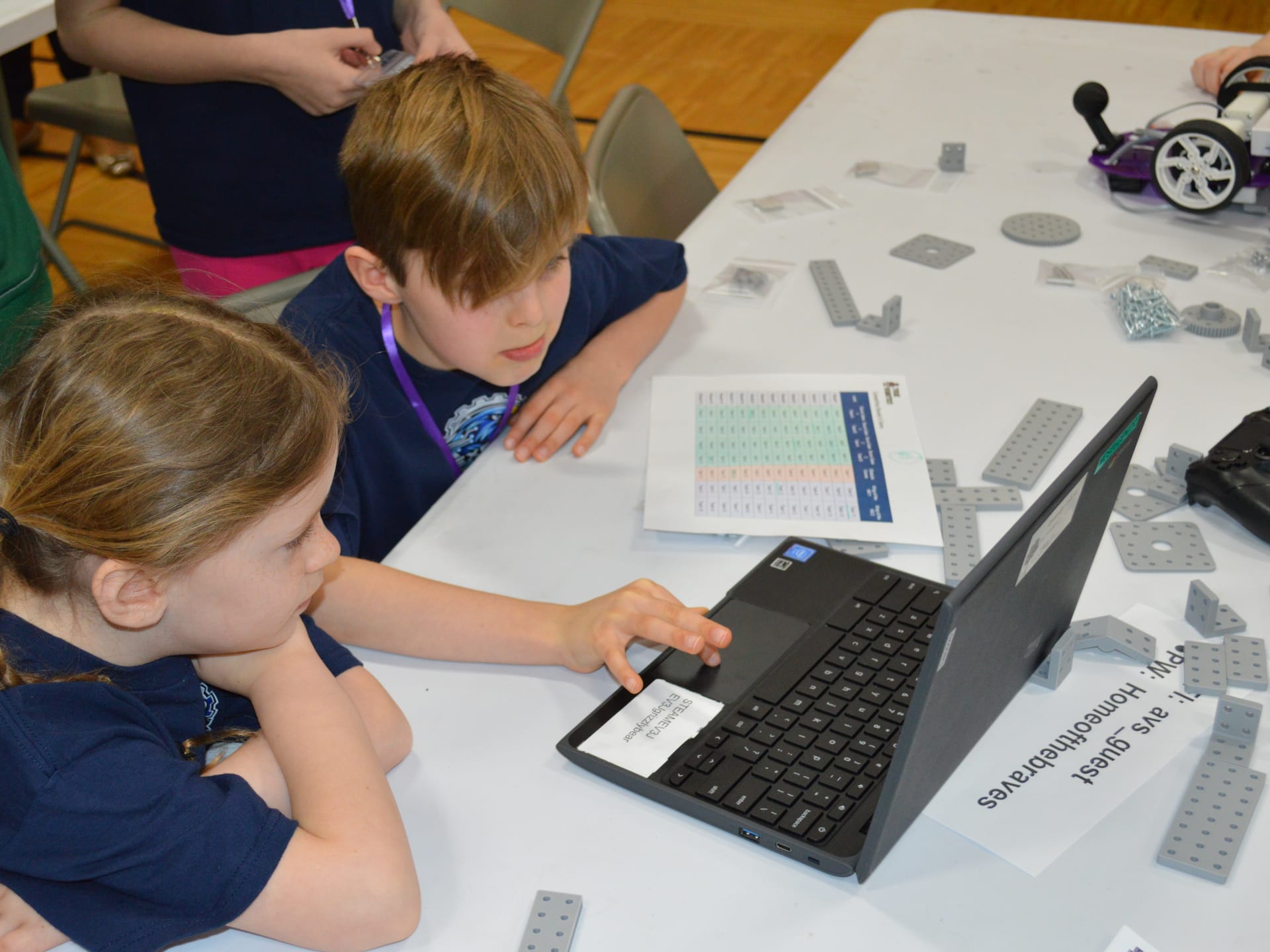Two students share a laptop to write their program while a Pilot robot and FlexForge plates wait on the table beside them