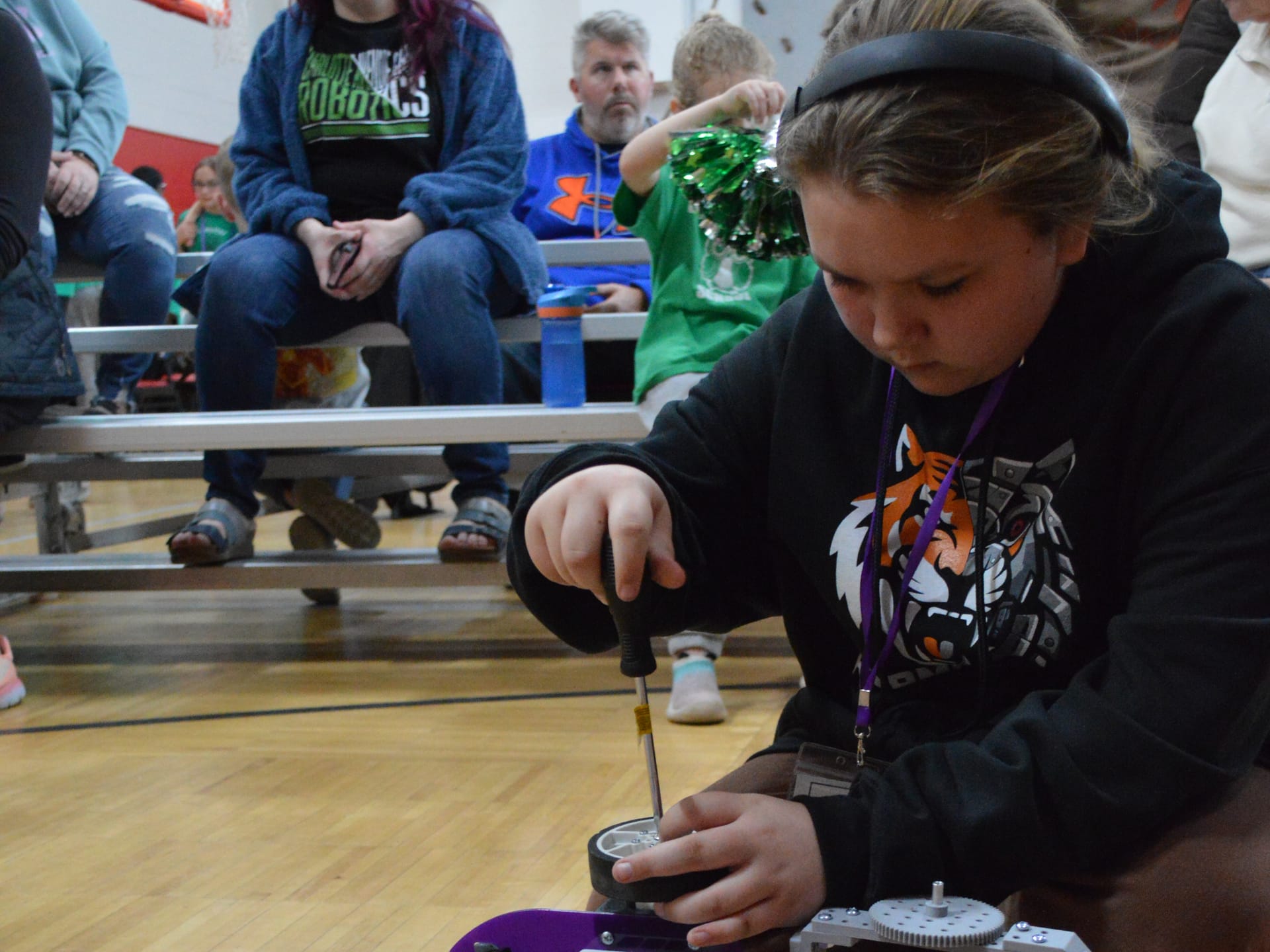 A student tightens a wheel onto a Pilot robot with a screwdriver beside the competition course